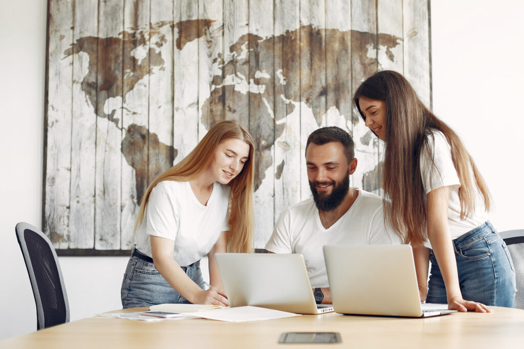 Team of young expats working on their laptops, with a world map on the background.